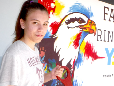 Sophia Pigman posa al lado del mural que diseñó y pintó en su escuela Faith Ringgold Arts & Science en Hayward.