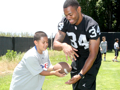 Oakland Raider George Atkinson III takes a handoff from a youngster participating in the NFL Play 60 Character Camp on the team’s practice field in Alameda. Atkinson and other Raider players mentored kids on life and football. Photo: Tony Gonzales/Raiders.com